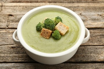 Tasty broccoli cream soup with croutons in bowl on wooden table, closeup
