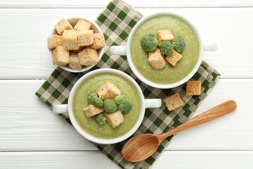 Tasty broccoli cream soup with croutons served on white wooden table, flat lay