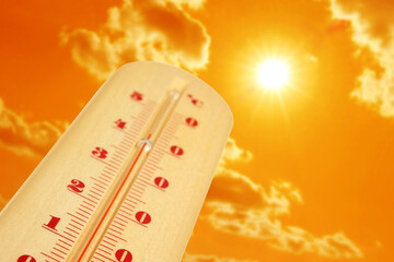 Thermometer showing high temperature against orange sky with bright sun and clouds. Extremely hot weather