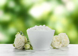 Sea salt in bowl and flowers on white marble table outdoors