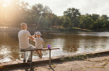 Father and young son fishing at calm lake in countryside at sunset. Horizontal family lifestyle photo with nature background and warm summer mood.