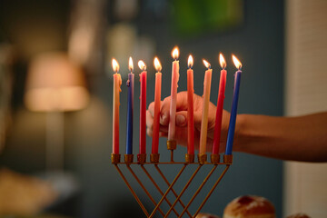 Hand lighting menorah candles during Hanukkah celebration, showing all nine candles burning...