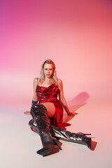 Elegant young blonde woman in a striking red dress poses in a vibrant studio setting