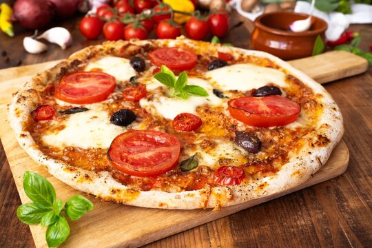 Delicious homemade Italian pizza with fresh tomato slices, melted mozzarella cheese, Kalamata olives and basil
