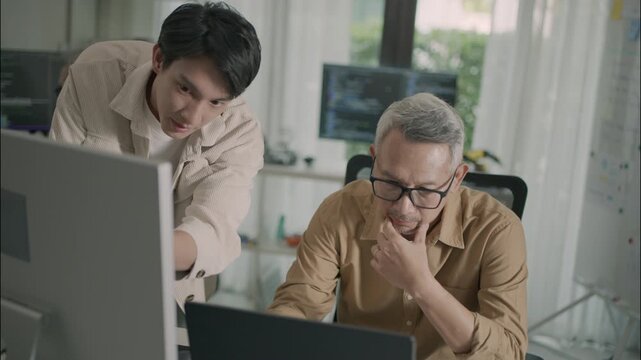 Asian senior student learning coding and AI technology with guidance from a young teacher having a computer, white board on background highlighting teamwork, digital skills, and intergenerational lear