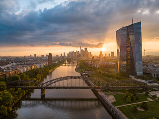 Aerial view of the sun's golden rays catching the glass facade of the European Central Bank and the steel latticework of bridges over the Main River, Frankfurt am Main, Hessen, Germany.