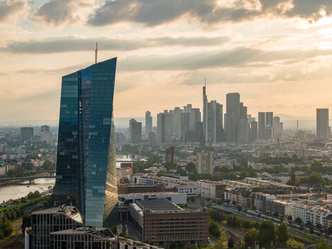 Aerial view of the modern, angled architecture of the European Central Bank building contrasting with the traditional Frankfurt skyline under a warm sky, Frankfurt am Main, Hessen, Germany.