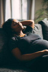 Fototapeta premium Pregnant woman resting comfortably on sofa, enjoying a moment of serenity and anticipation during her pregnancy journey in a cozy setting.