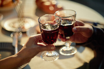 Woman and man clinking wine glasses during Hanukkah celebration, hands visible holding glasses filled with red wine, festive table setting in background