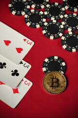 A red felt table with three of a kind or set playing cards and black and white poker chips against the backdrop of a shining golden Bitcoin coin during an exciting casino game