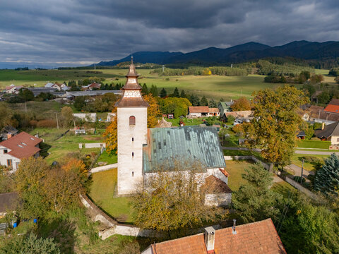 Aerial view of the stone church rising amidst the autumn-tinged trees, contrasting against the distant mountains and moody sky, H&Atilde;&iexcl;j, &Aring;&frac12;ilina Region, Slovakia.