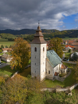 Aerial view of a medieval church with a towering spire, its stone walls glowing softly under the diffused autumn light, H&Atilde;&iexcl;j, &Aring;&frac12;ilina Region, Slovakia.