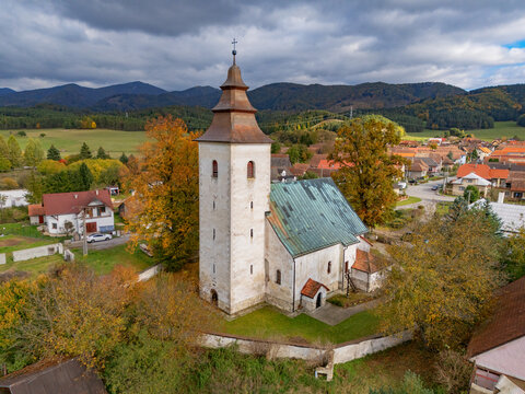 Aerial view of the ancient church with its weathered steeple piercing the sky, framed by autumn's fiery hues against the backdrop of distant mountains, H&Atilde;&iexcl;j, &Aring;&frac12;ilina Region, Slovakia.