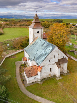 Aerial view of the ancient, weathered church with its weathered stone walls, copper-green roof, and rustic tower, standing proudly amidst golden autumn trees, H&Atilde;&iexcl;j, &Aring;&frac12;ilina Region, Slovakia.