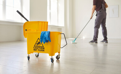 Yellow mop bucket with Caution Wet Floor sign with blue cloth and mop, man mopping empty room performing cleaning task, cleaning service and maintenance indoor, sanitizing, commercial janitorial © Studio Romantic