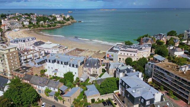 Sunny aerial of Plage de l&rsquo;Ecluse with umbrellas, clear turquoise water, and beach activity, aerial pullback