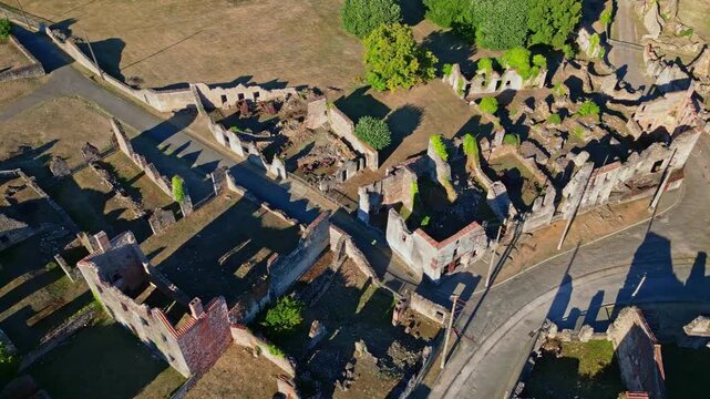 Aerial of ruined buildings and empty streets in WWII memorial site Oradour sur Glane, France, tracking right textured with long shadows