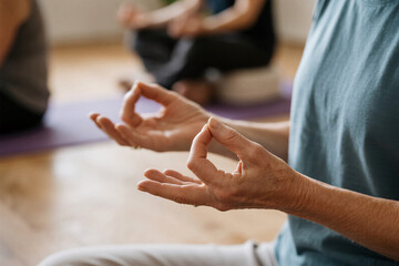 Obraz premium Elderly woman’s hands in meditation mudra close-up with soft blurred yoga studio, symbolizing mindfulness and dementia prevention for healthy aging and inner peace