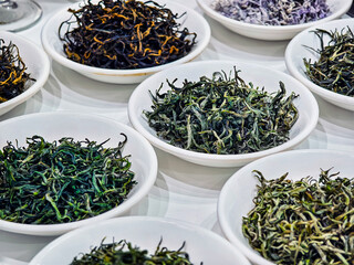 Various types of loose leaf tea displayed in white bowls at a tea shop during a sunny afternoon
