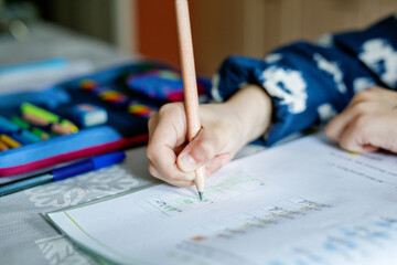 Cute elementary school girl sitting at a desk at home, writing in her workbook and doing school homework. Focused child learning and studying indoors. Concept of education, childhood, home learning.