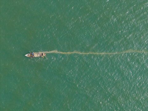 Fishing boat laying out a long net in the vibrant green sea, palomino beach, guajira, colombia