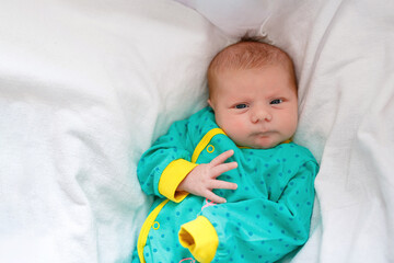 Cute adorable newborn baby in white bed and wrapped in blanket. New born child, little girl looking surprised at the camera. Family, new life, childhood, beginning concept