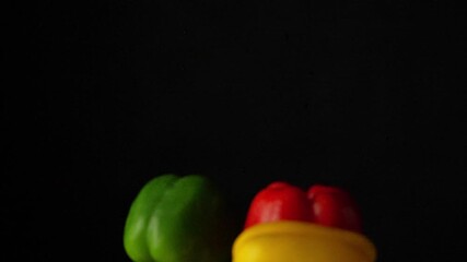 Slow motion shot of fresh bell peppers falling and bouncing towards camera on black background. Premium vegetable footage perfect for cooking shows and restaurant marketing content. - Powered by Adobe
