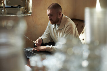 Caucasian young adult man sitting on sofa working on laptop while holding document, focused...