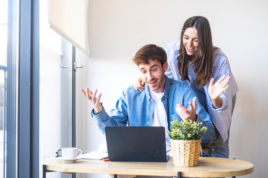 Smiling young man and woman working together at home office desk with laptop. Happy colleagues or couple collaborating on project, representing teamwork, remote work, startup success and modern busine