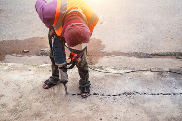 Construction Worker Making Repairs on Sidewalk with Electric Jackhammer in Safety Vest and Helmet during Daytime Work in Urban Area