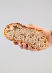 Man's hand holding a slice of bread on a grey background.