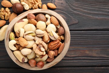 Mix of different nuts in bowl on wooden table, flat lay. Space for text