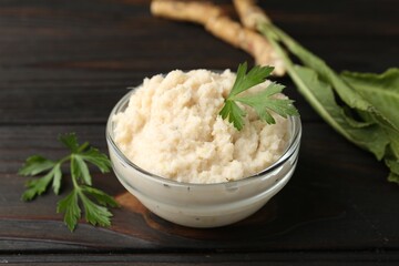 Tasty horseradish sauce with parsley and roots on black wooden table, closeup