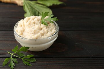Tasty horseradish sauce with parsley and roots on black wooden table, closeup. Space for text