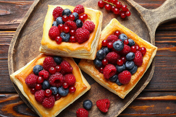Tasty puff pastries with berries on wooden table, top view