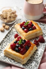 Tasty puff pastries with berries, mint, brown sugar and coffee on table, closeup