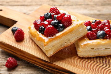 Tasty puff pastries with berries on wooden table, closeup