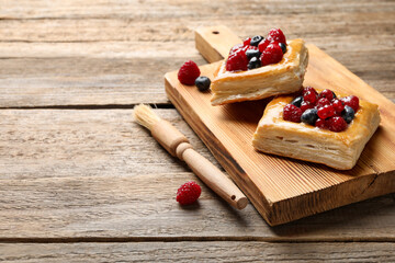 Tasty puff pastries with berries and brush on wooden table, closeup. Space for text