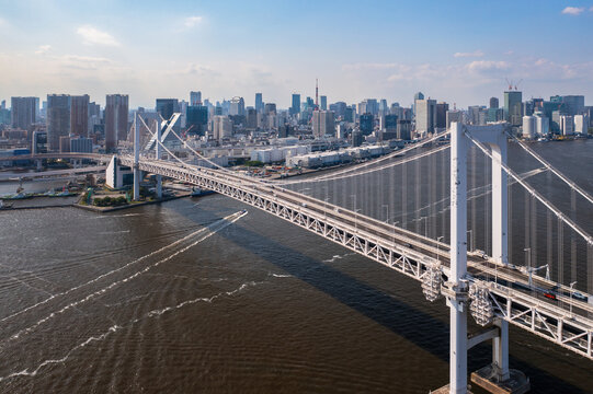 Aerial view of the Rainbow Bridge stretching over the dark water, contrasting with the bright city skyline and blue sky, Tokyo, Tokyo, Japan.