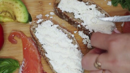 a woman cooks at home salmon and avocado sandwich cottage cheese or soft cheese whole wheat bread....
