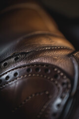 Detailed shot of brown leather dress shoe with stitching and brogue detailing, showcasing craftsmanship and luxury. Focus on textures.