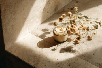 Natural skincare: glass jar of cream and dried flowers in the sunlight on stone steps. Spa aesthetic.