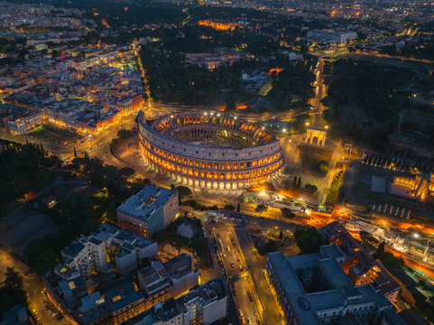 Aerial view of the illuminated Colosseum standing majestically amidst the ancient city's warm glow, a testament to enduring history, Roma, Lazio, Italy.