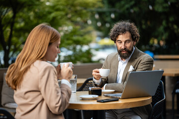 Business people having coffee and discussing work on laptop in outdoor cafe