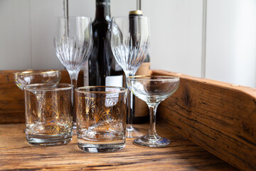 A close-up collection of patterned tumblers, champagne glasses, and wine glasses is displayed with wine bottles on a rustic wooden sideboard. Graphic resource.