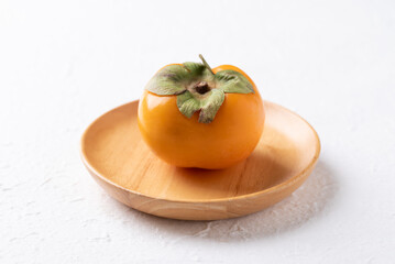 Fresh ripe persimmon on wooden plate with white background, Autumn sweet fruit