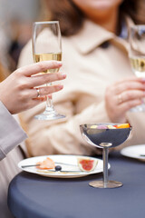 Woman holding a glass of sparkling wine, plate with fig and snacks on table, party atmosphere.