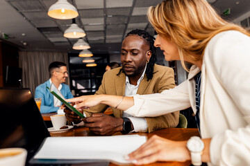 Businessman and female coworker talking about work while using laptop in modern coffee shop.