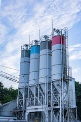 Tall industrial silos with colorful tops standing against blue cloudy sky