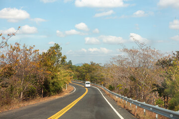 The empty asphalt road curves through the autumn forest landscape, a country way beckoning travel beneath the horizon sky